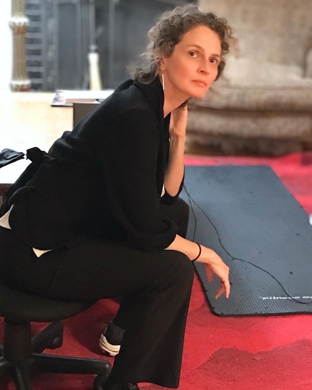 Jessica Cuello, a white woman dressed in black, sits with her elbow on her knee and her head in her hand. She faces the camera.